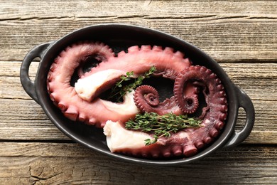 Fresh raw octopus and thyme in baking dish on wooden table, top view