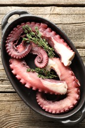 Photo of Fresh raw octopus and thyme in baking dish on wooden table, top view