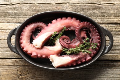 Photo of Fresh raw octopus and thyme in baking dish on wooden table, top view