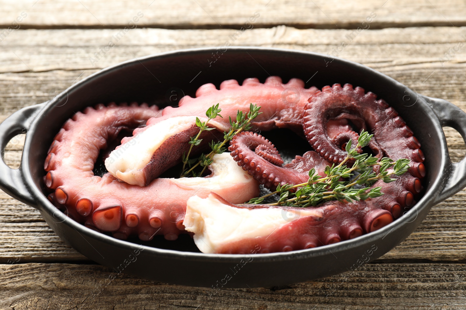 Photo of Fresh raw octopus and thyme in baking dish on wooden table, closeup