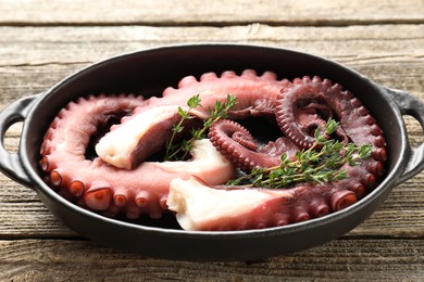 Photo of Fresh raw octopus and thyme in baking dish on wooden table, closeup