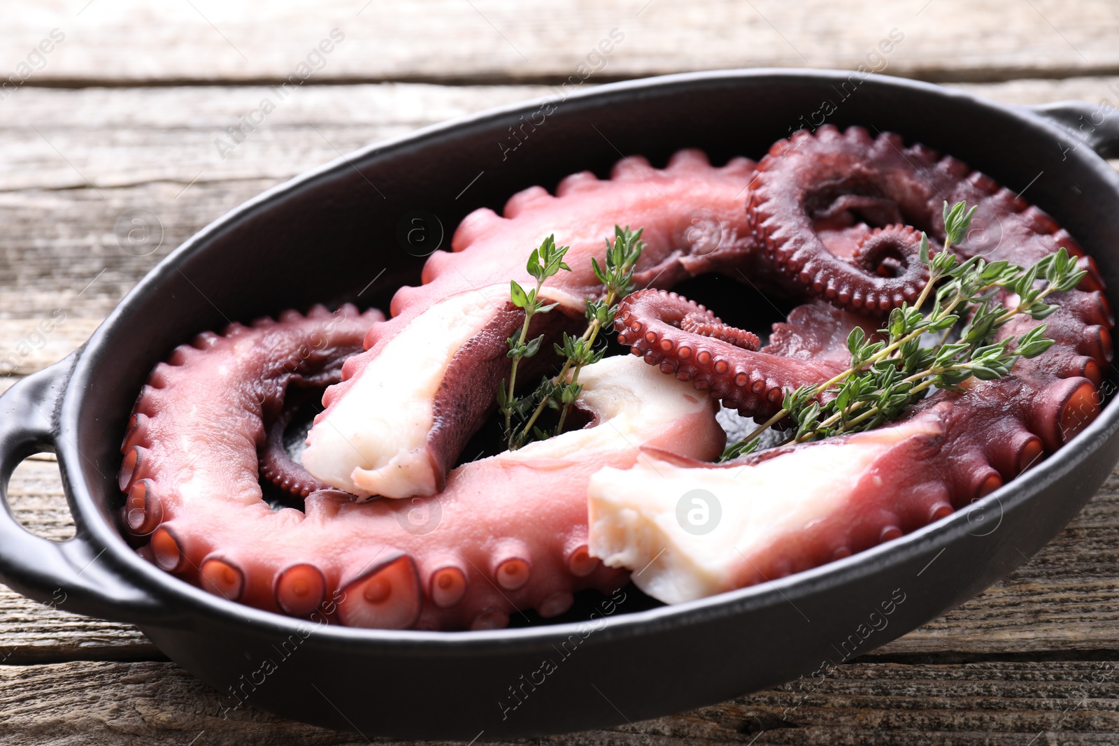 Photo of Fresh raw octopus and thyme in baking dish on wooden table, closeup