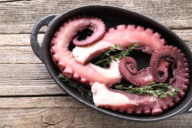 Photo of Fresh raw octopus and thyme in baking dish on wooden table, top view