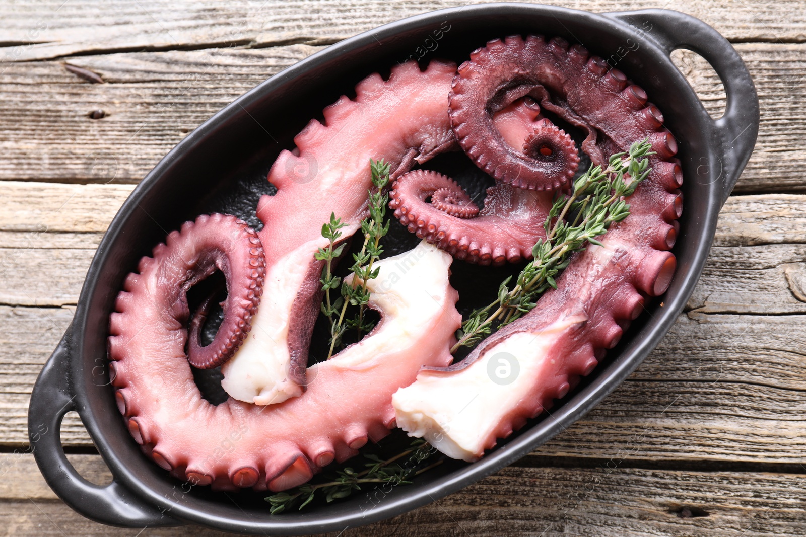 Photo of Fresh raw octopus and thyme in baking dish on wooden table, top view