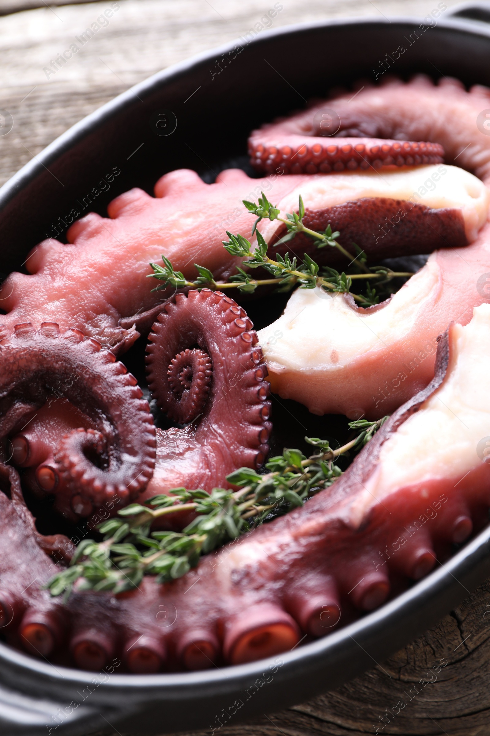 Photo of Fresh raw octopus and thyme in baking dish on table, closeup