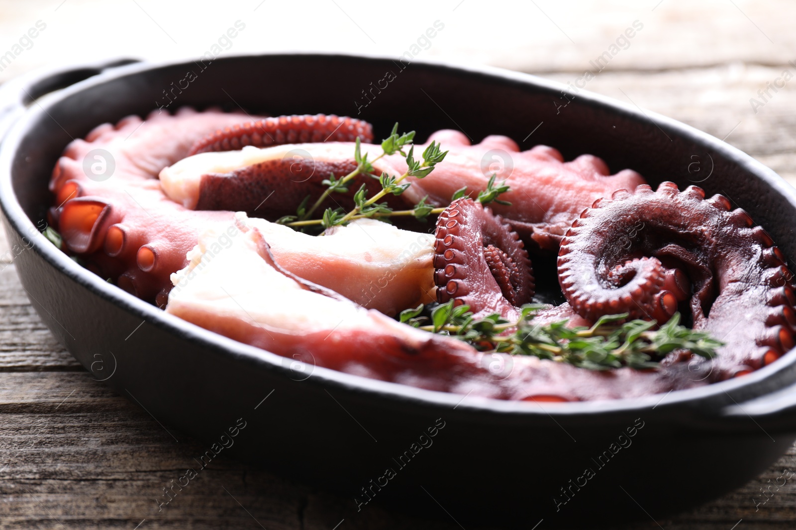 Photo of Fresh raw octopus and thyme in baking dish on wooden table, closeup