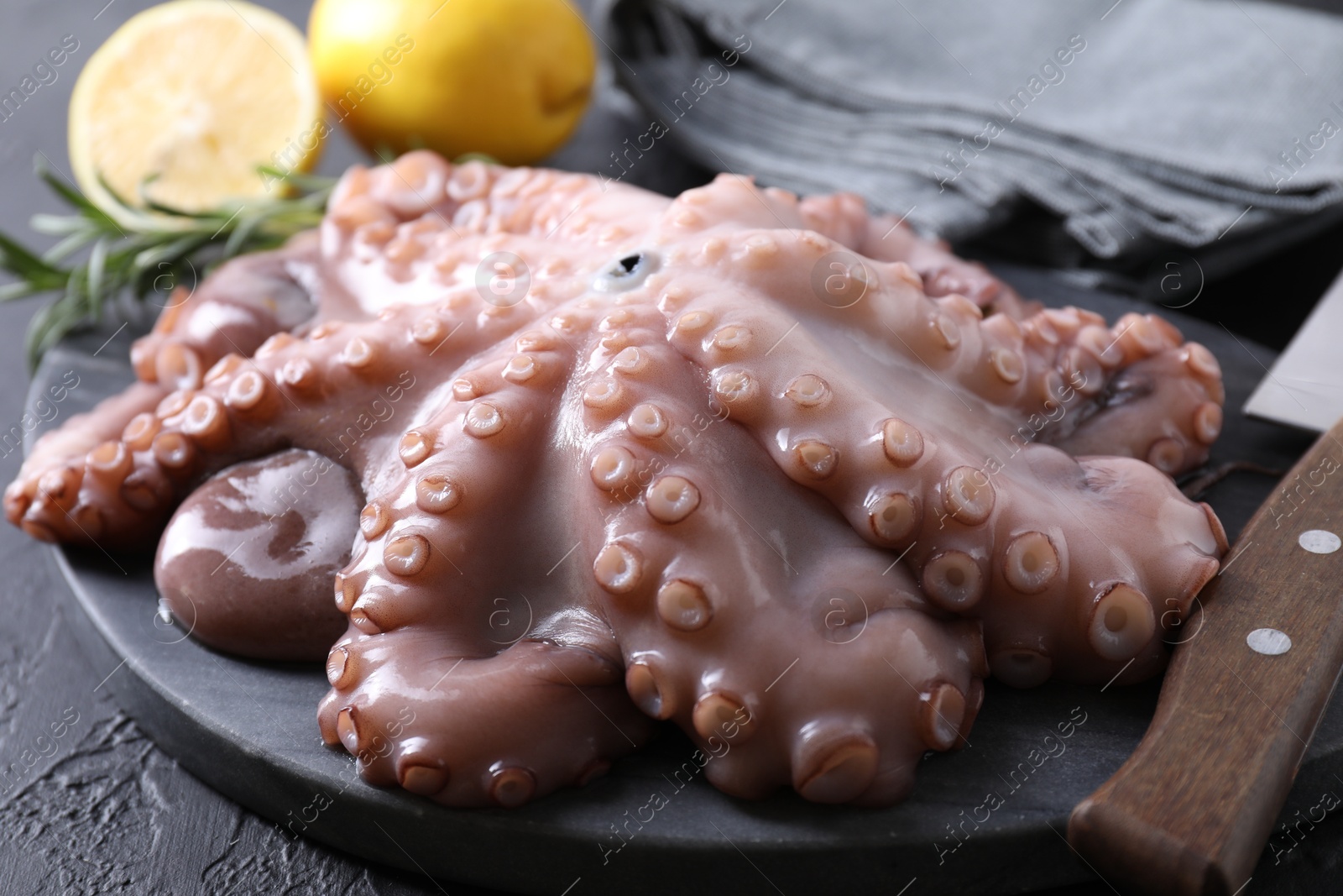 Photo of Fresh raw octopus, lemon, rosemary and knife on black table, closeup