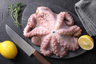 Photo of Fresh raw octopus, lemon, rosemary and knife on black table, top view