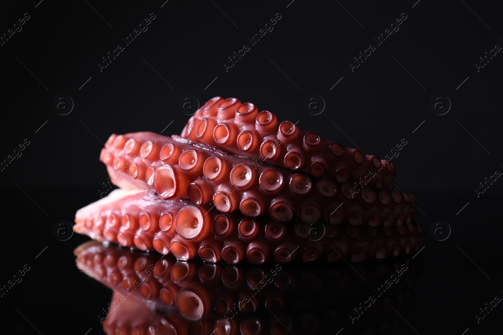 Photo of Cut fresh raw octopus on black mirror surface