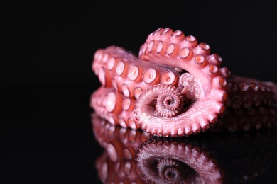 Photo of Cut fresh raw octopus on black mirror surface, closeup. Space for text