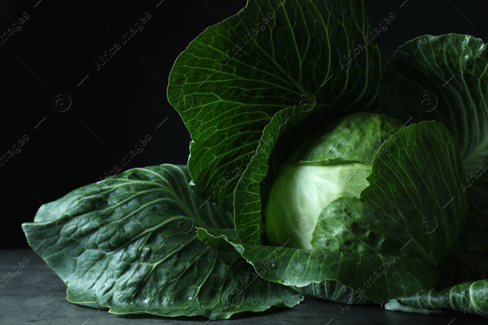 Photo of Whole ripe head of cabbage on table against dark background, closeup