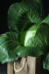 Photo of Whole ripe head of cabbage in wooden crate on dark background, closeup