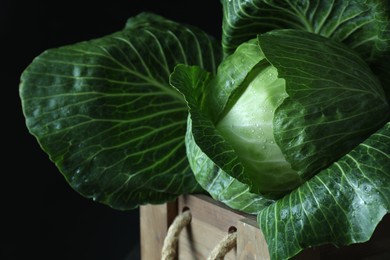 Photo of Whole ripe head of cabbage in wooden crate on dark background, closeup