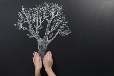 Photo of Woman pretending to hold tree drawn on chalkboard, closeup. Space for text