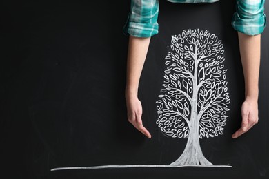 Photo of Woman keeping safe tree drawn on chalkboard, closeup. Space for text