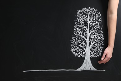 Photo of Woman keeping safe tree drawn on chalkboard, closeup. Space for text