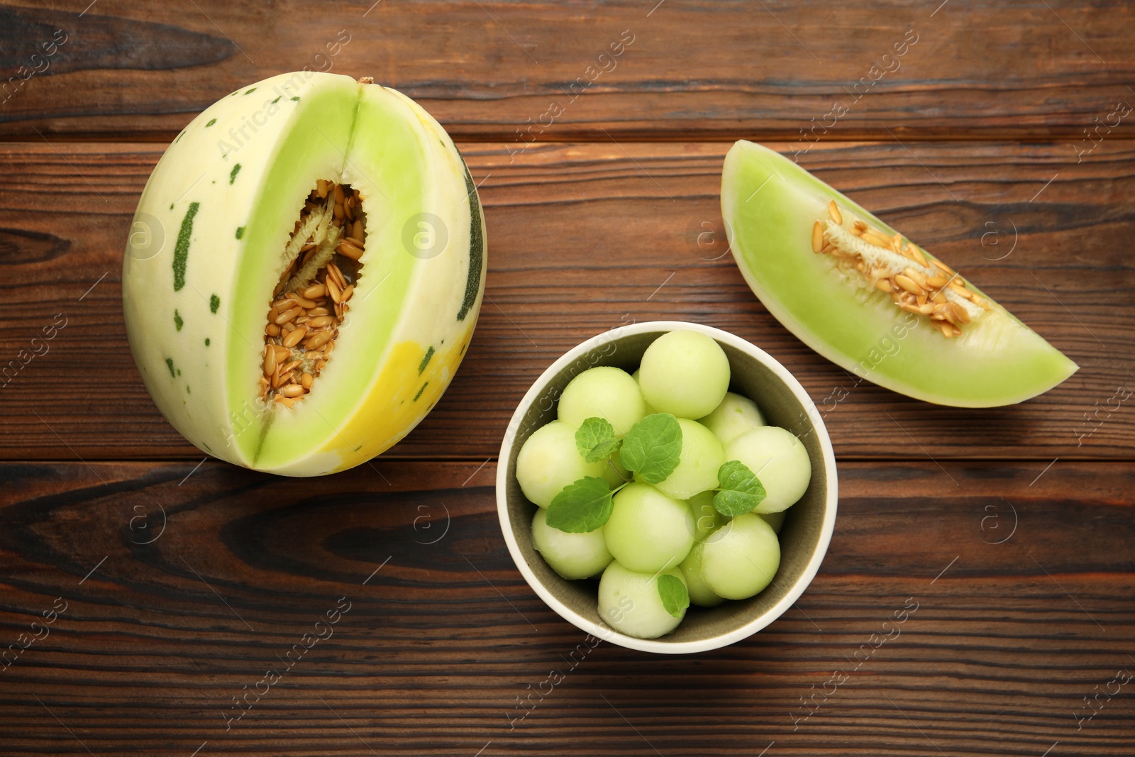 Photo of Melon balls in bowl and fresh fruit on wooden table, flat lay