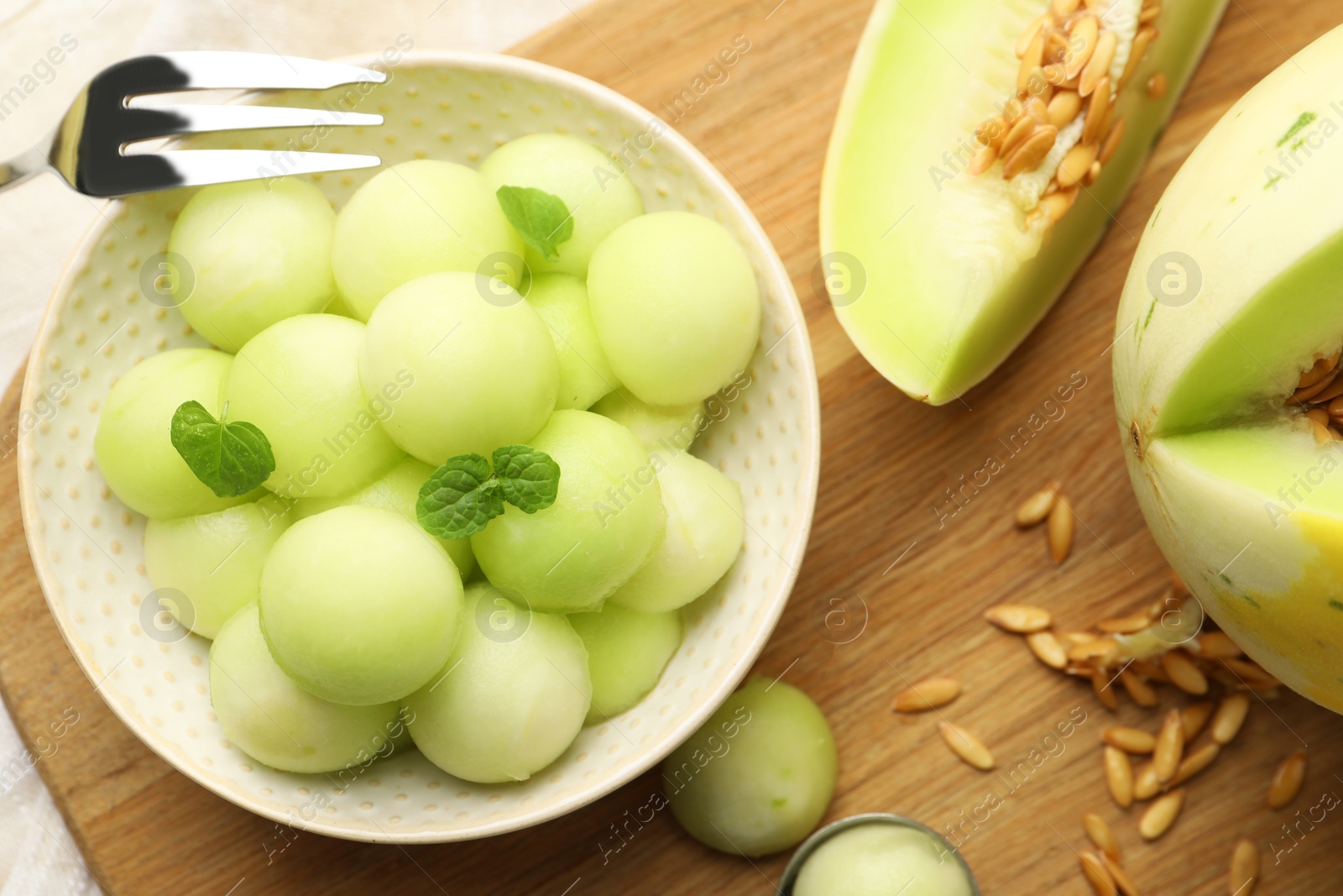 Photo of Melon balls in bowl and fresh fruit on wooden board, flat lay