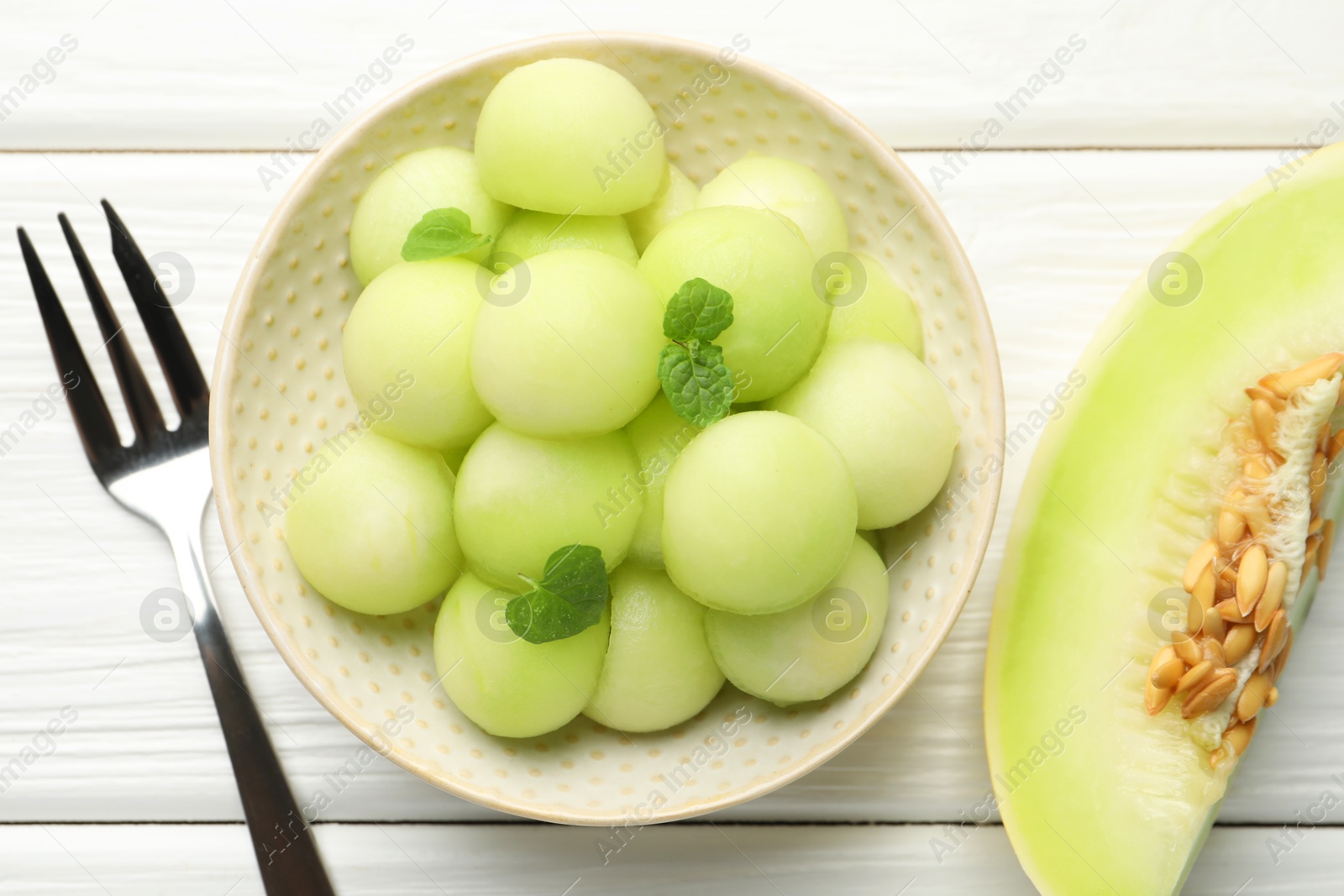 Photo of Melon balls in bowl and fresh fruit on wooden table, top view