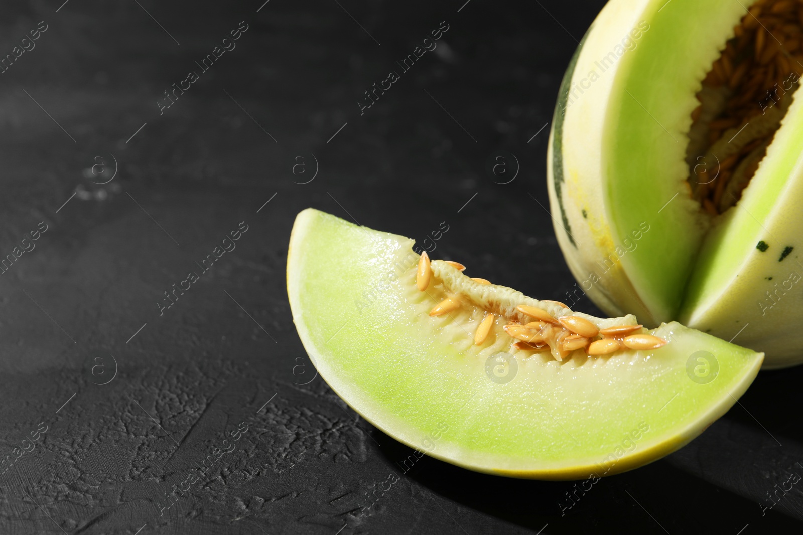 Photo of Fresh ripe honeydew melon on dark table, closeup. Space for text