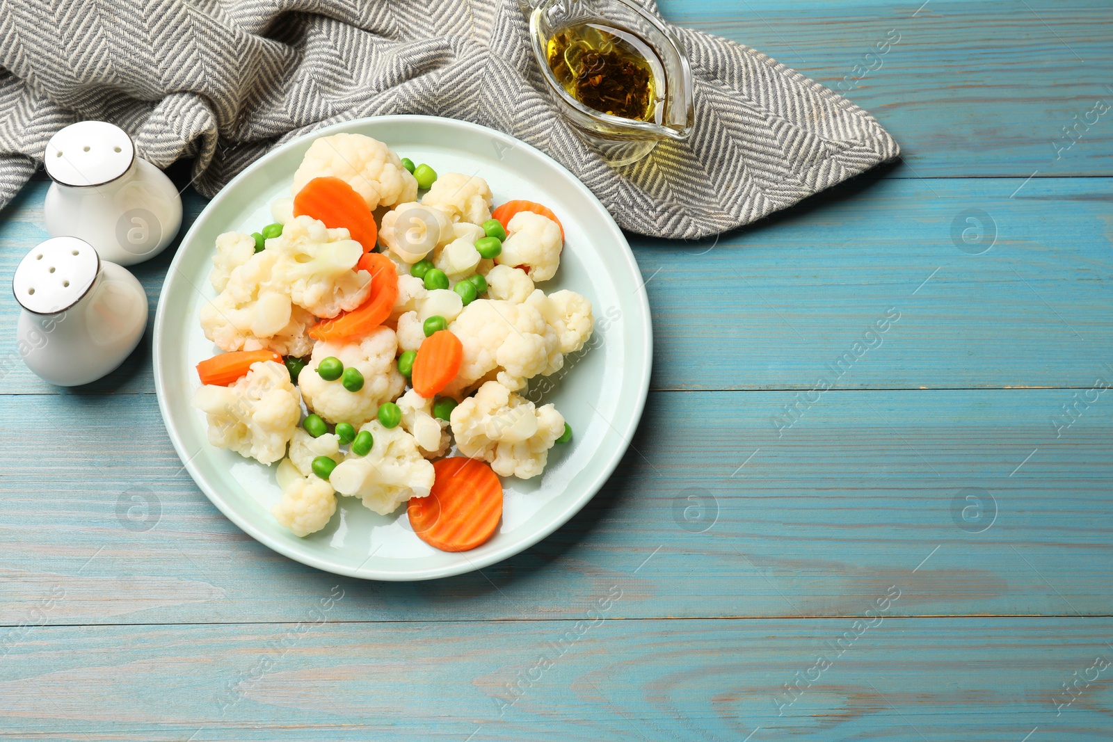 Photo of Tasty cooked cauliflower with green peas and carrot slices served on light blue wooden table, flat lay. Space for text