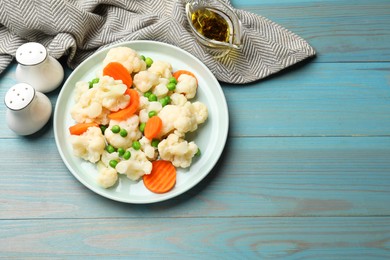 Photo of Tasty cooked cauliflower with green peas and carrot slices served on light blue wooden table, flat lay. Space for text