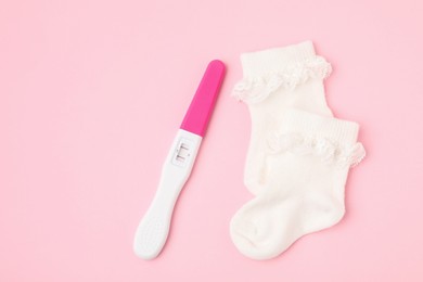 Photo of Pregnancy test and socks on pink background