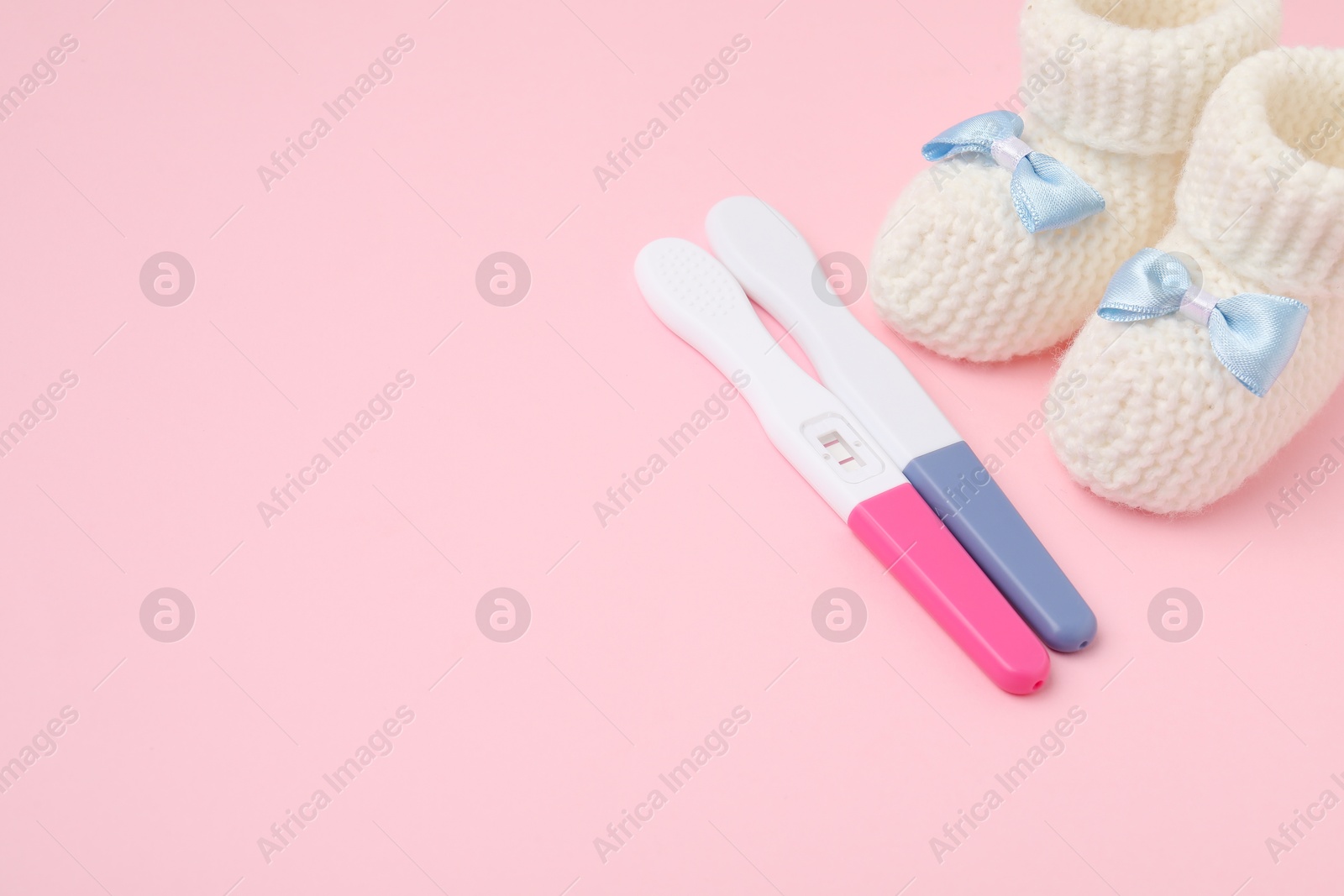 Photo of Pregnancy tests and knitted booties on pink background, space for text