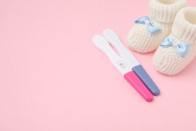 Photo of Pregnancy tests and knitted booties on pink background, space for text