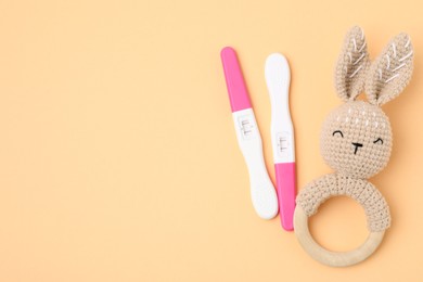 Photo of Pregnancy tests and baby rattle on pale orange background, top view. Space for text