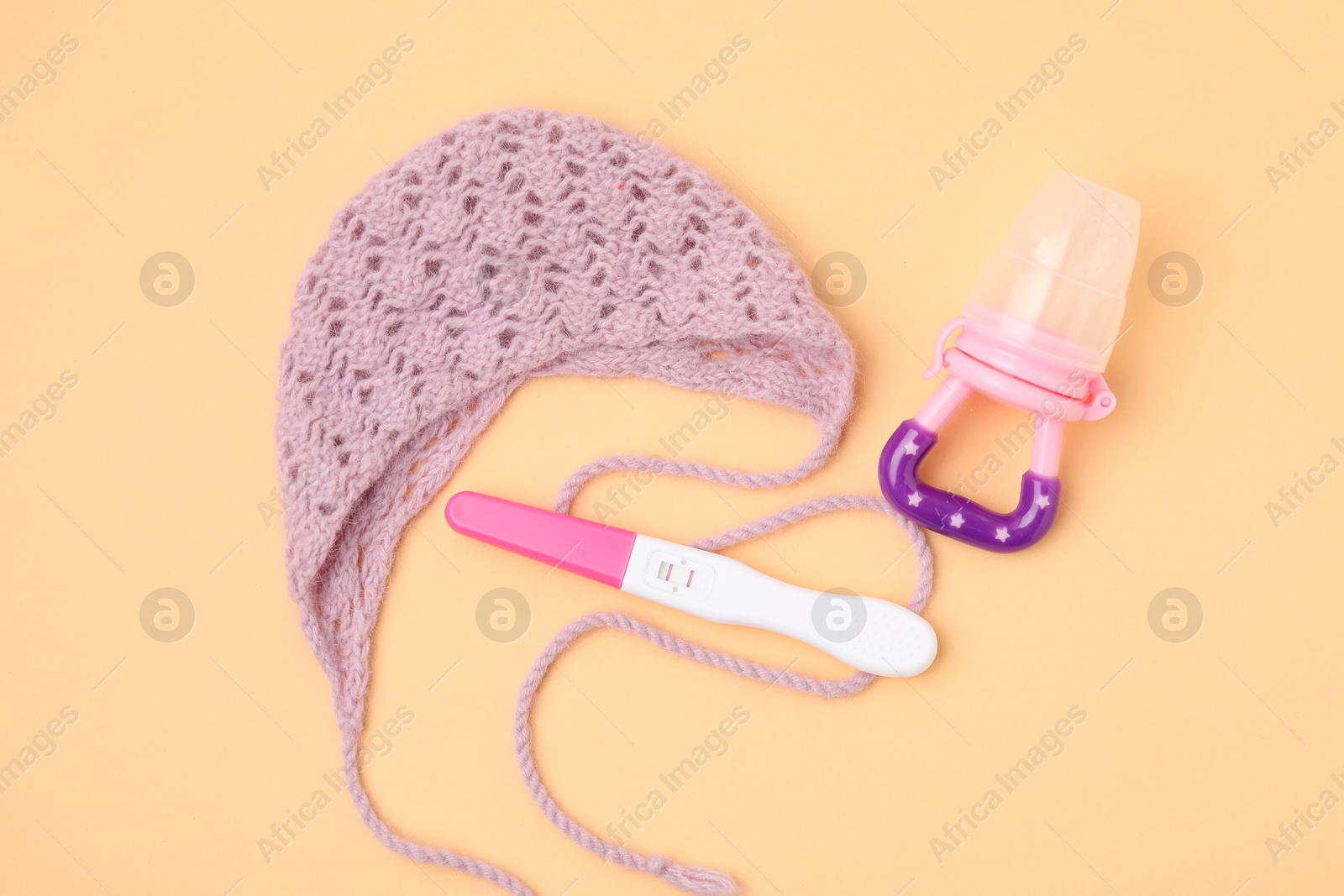 Photo of Pregnancy test, nibbler and knitted hat on pale orange background, top view