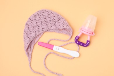 Photo of Pregnancy test, nibbler and knitted hat on pale orange background, top view