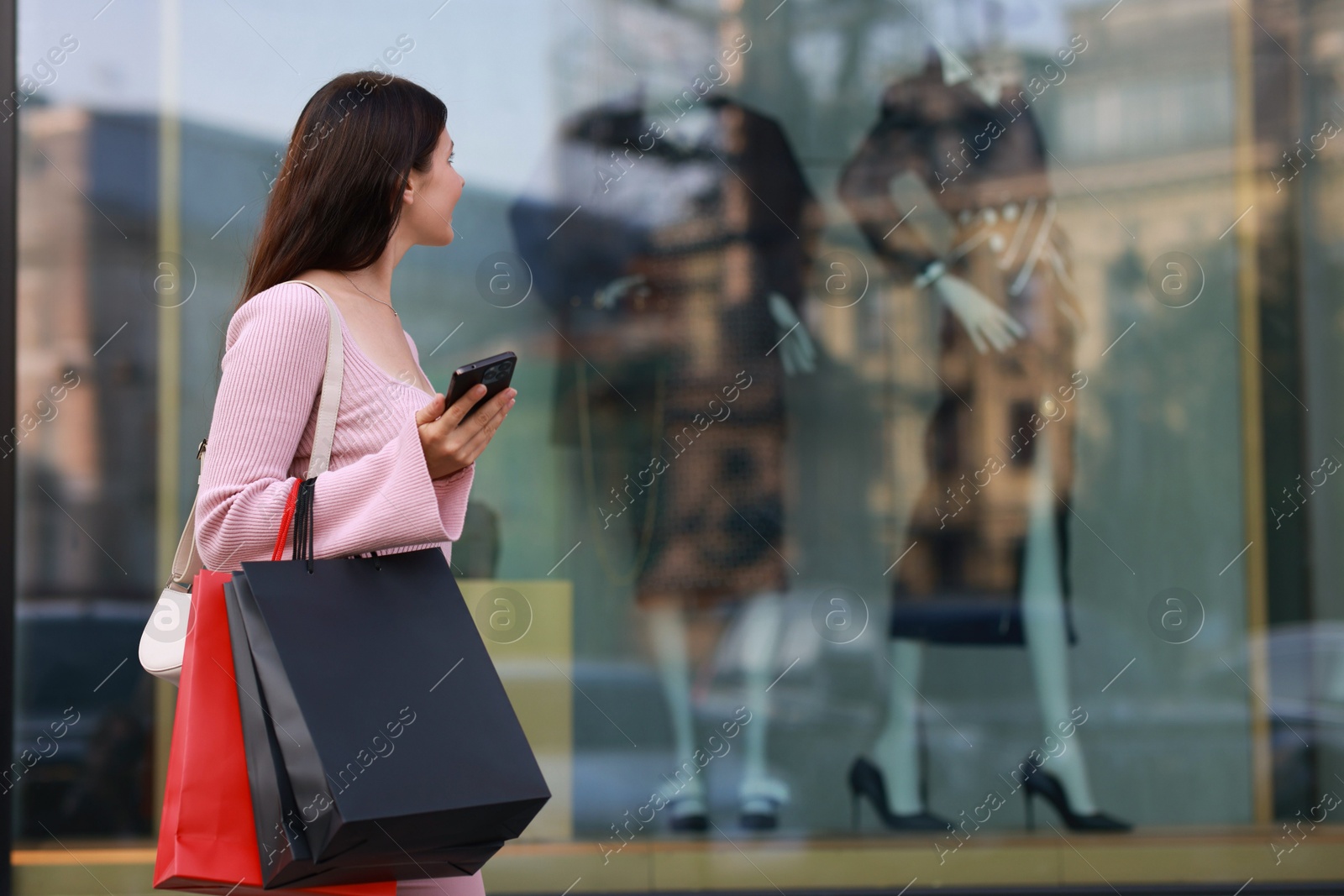 Photo of Woman with colorful shopping bags using smartphone outdoors, space for text