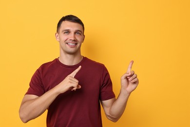 Photo of Smiling man with dental braces pointing at something on yellow background. Space for text