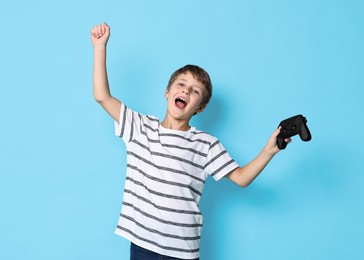 Photo of Cute little boy with controller on light blue background