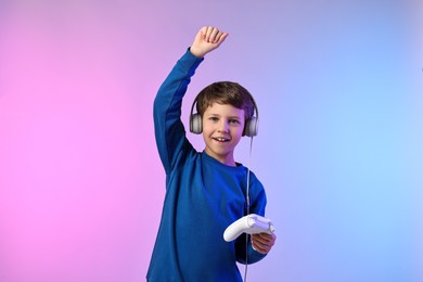 Happy little boy in headphones with controller on color background