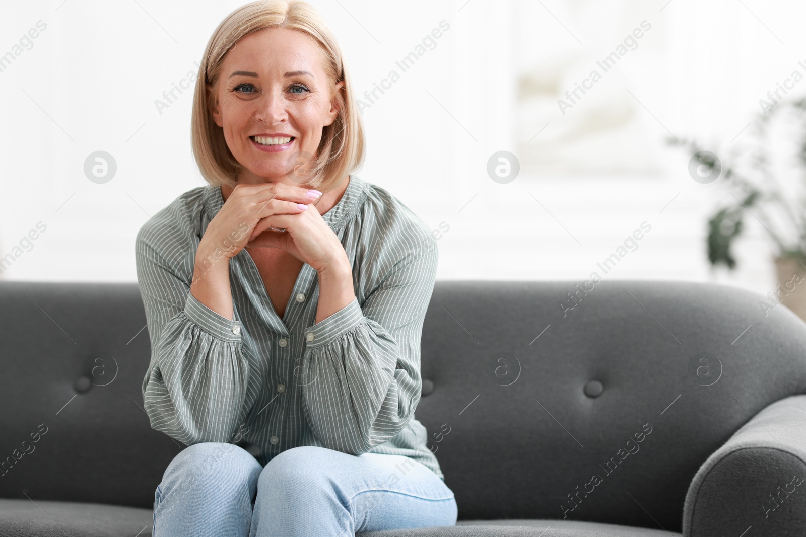 Photo of Happy middle aged woman on sofa indoors, space for text