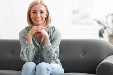 Photo of Happy middle aged woman on sofa indoors, space for text