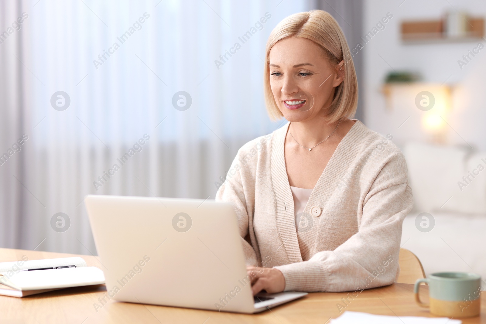 Photo of Happy middle aged woman using laptop at table indoors