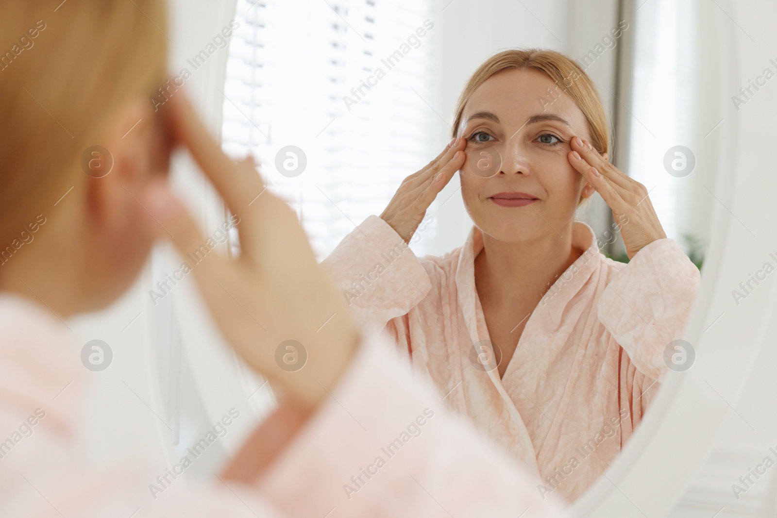 Photo of Beautiful woman doing facial self massage near mirror in bathroom