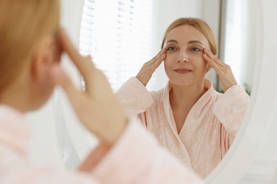 Beautiful woman doing facial self massage near mirror in bathroom