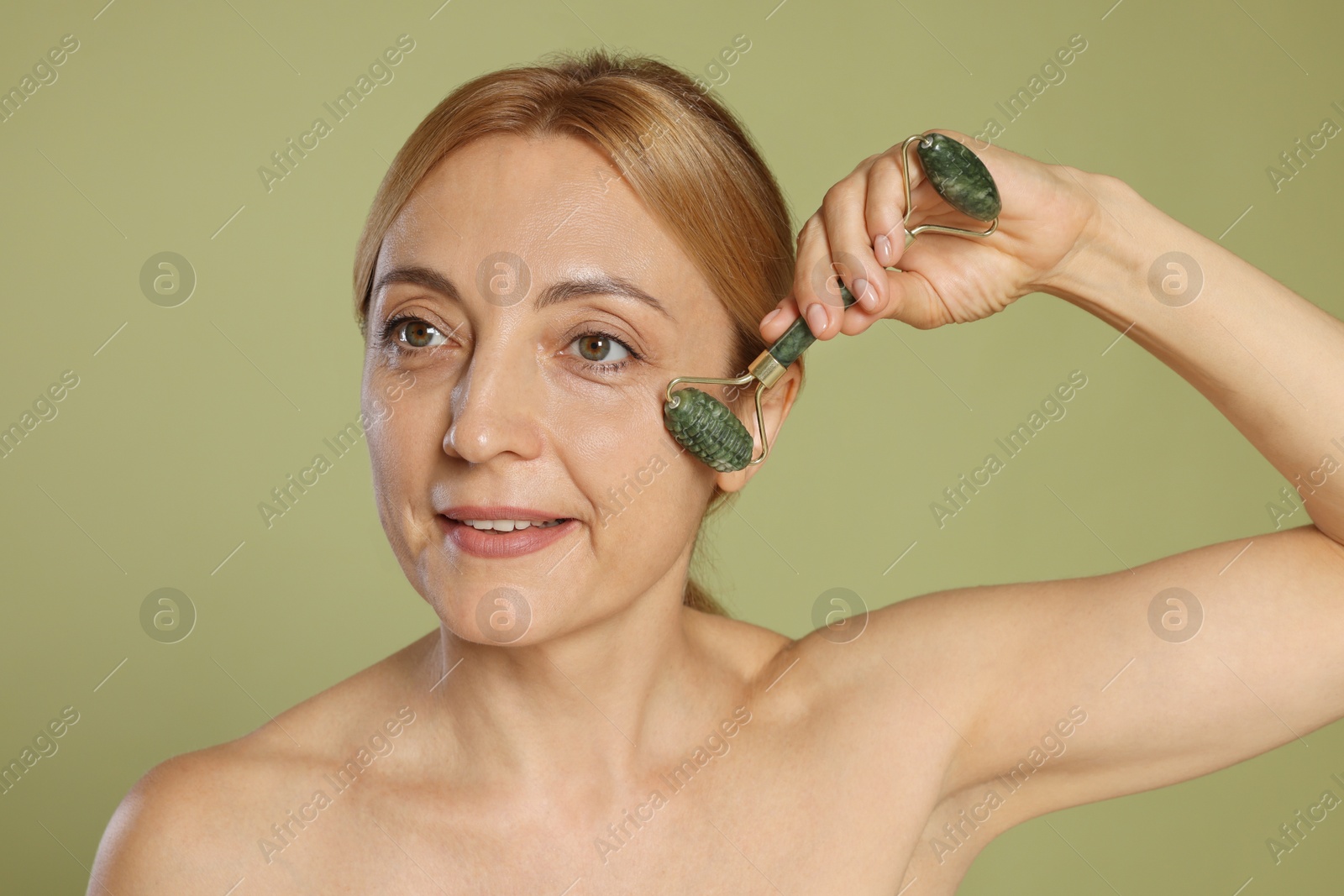 Photo of Beautiful woman doing facial self massage with roller on green background