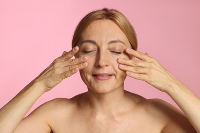 Beautiful woman doing facial self massage on pink background