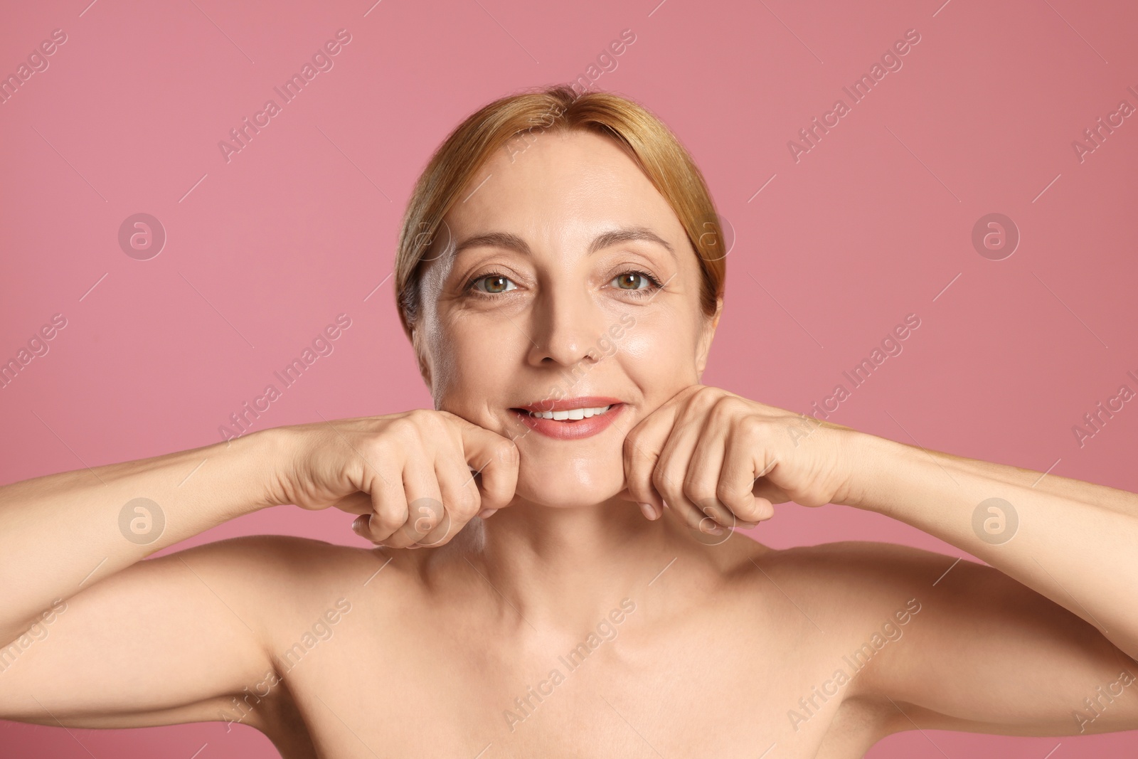 Photo of Smiling woman doing facial self massage on pink background