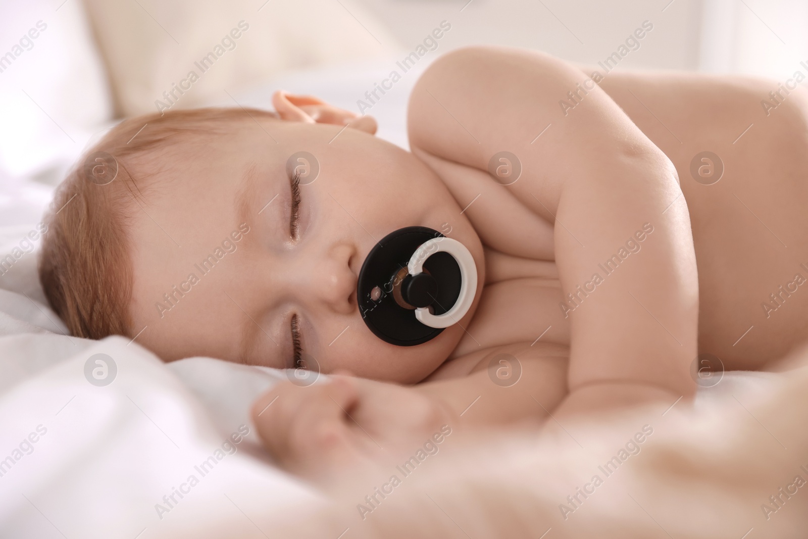 Photo of Cute little baby with pacifier sleeping on bed at home