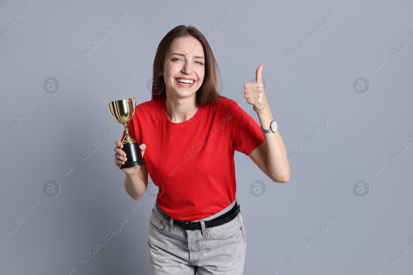 Photo of Happy winner with gold trophy cup showing thumbs up on gray background