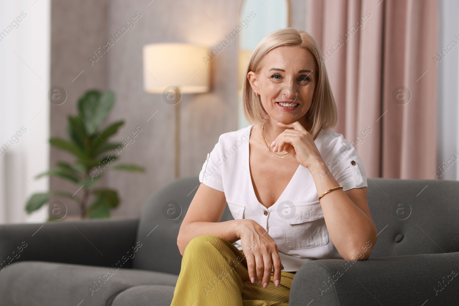 Photo of Portrait of smiling middle aged woman on sofa at home. Space for text