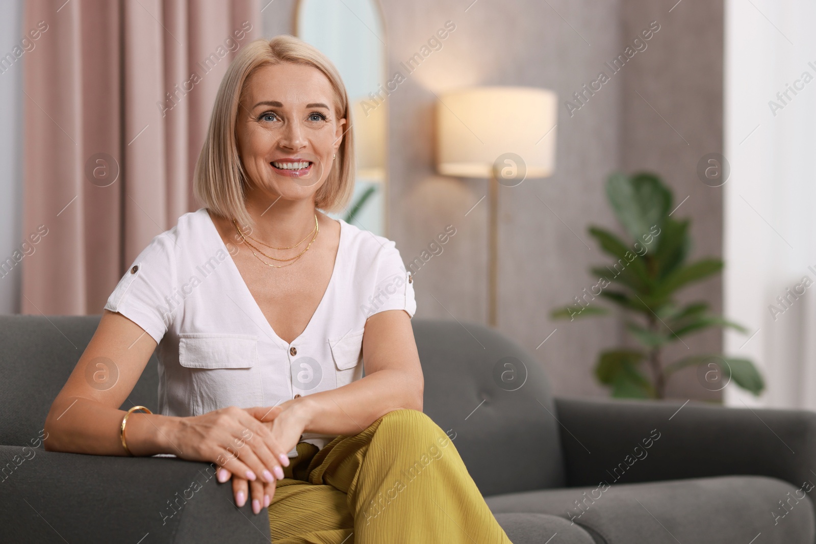 Photo of Portrait of smiling middle aged woman on sofa at home. Space for text