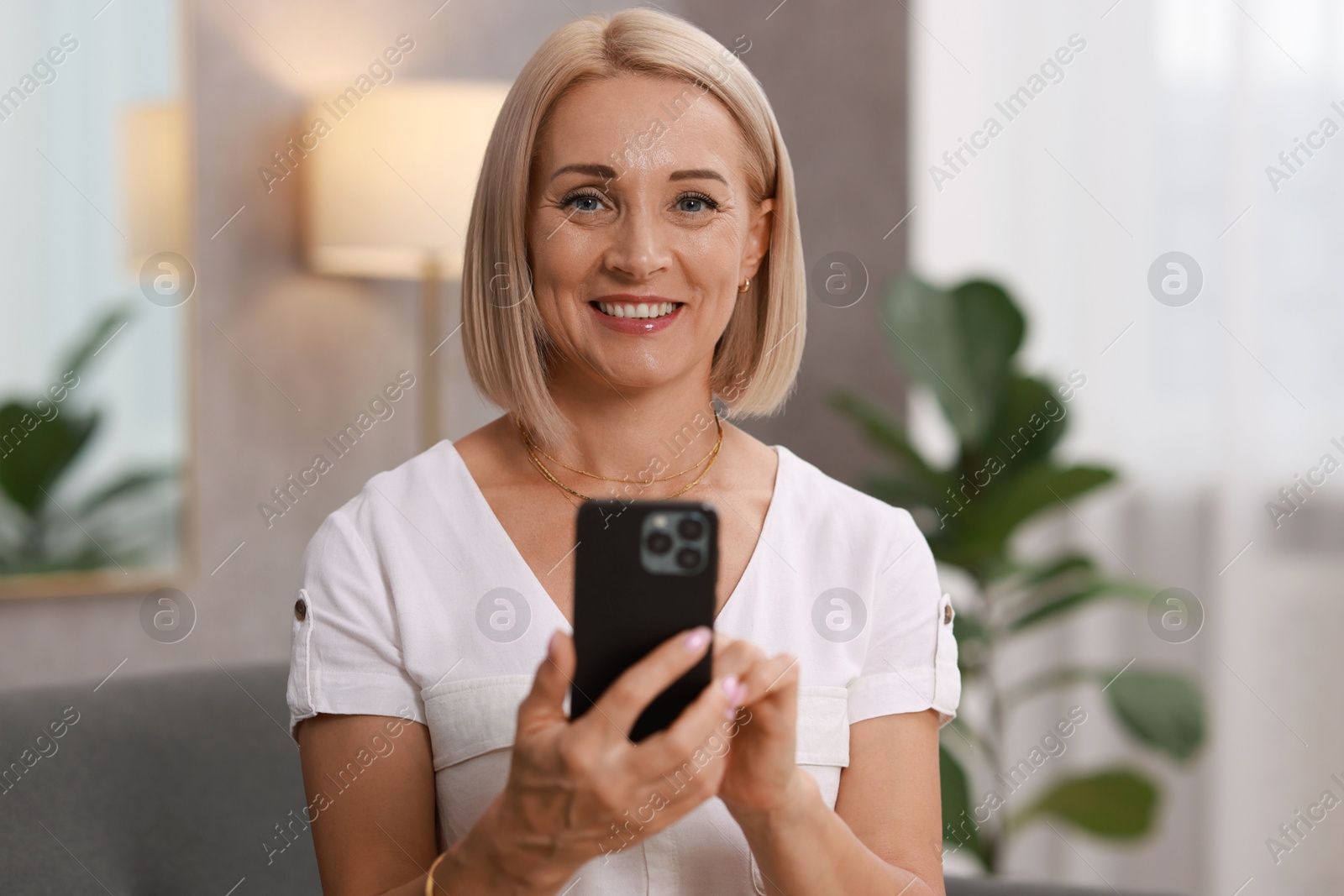 Photo of Portrait of smiling middle aged woman with smartphone at home