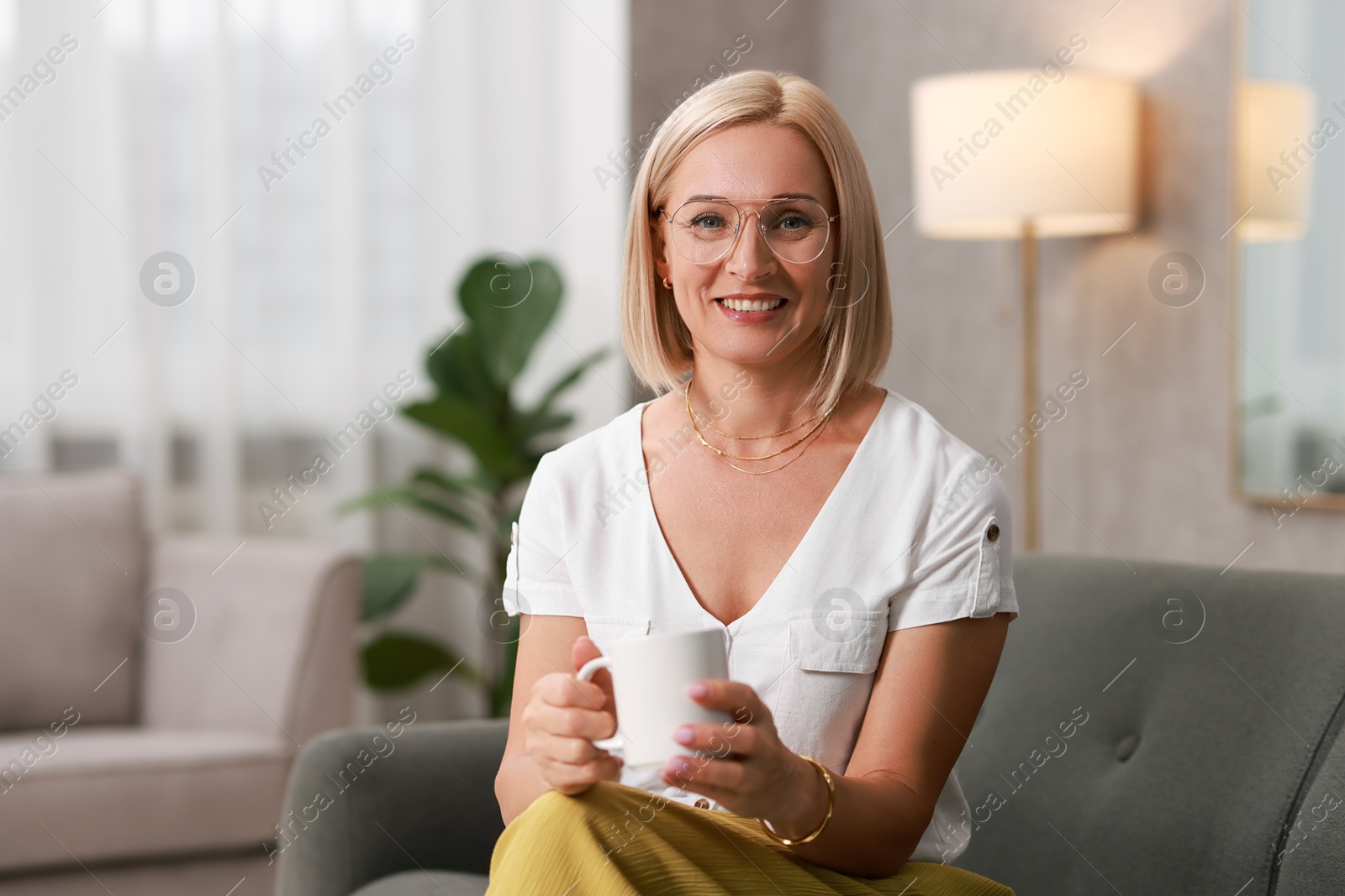 Photo of Smiling middle aged woman with cup of hot drink on sofa at home